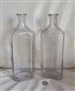 Vintage clear glass apothecary storage bottles pair showing measurement scales and 3xxxii shoulder markings