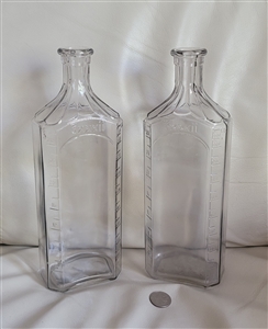 Vintage clear glass apothecary storage bottles pair showing measurement scales and 3xxxii shoulder markings