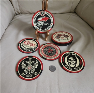 Four circular Shepard Fairey OBEY GIANT coasters with various street art designs displayed alongside their red and black metal storage tin