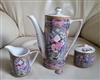 Three piece Japanese porcelain tea service with pink roses and gold mythical griffin patterns including lidded teapot sugar and creamer