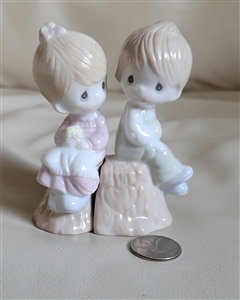 The front view shows the 1993 Precious Moments boy and girl salt and pepper shakers sitting on logs with a coin for size comparison.