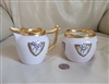 An antique Theodore Haviland Limoges porcelain creamer and open sugar bowl feature a soft pink background with gold and black medallions containing lotus floral designs alongside heavy gold rims and handles