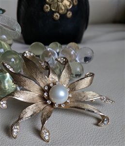 Vintage BSK satin gold tone floral brooch featuring sweeping petals, clear crystals, and central faux pearl