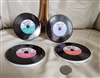 Four circular glass coasters shaped like vinyl records with colorful center labels and realistic grooves