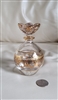 Detailed close up view of an Italian Royal Limited 24 percent lead crystal perfume bottle featuring hand painted gold gilded floral decor a matching sculptural floral stopper and a coin for scale resting on a white surface