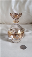 Detailed close up view of an Italian Royal Limited 24 percent lead crystal perfume bottle featuring hand painted gold gilded floral decor a matching sculptural floral stopper and a coin for scale resting on a white surface