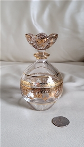 Detailed close up view of an Italian Royal Limited 24 percent lead crystal perfume bottle featuring hand painted gold gilded floral decor a matching sculptural floral stopper and a coin for scale resting on a white surface