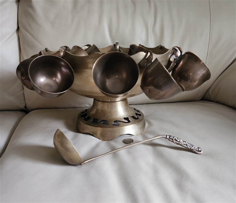 Vintage brass punch bowl set with pedestal base, ornate matching ladle, and twelve hanging cups showcasing natural patina and detailed cut-out craftsmanship