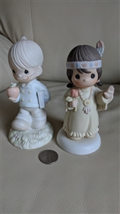 The front view shows the 1992 Bless-Um You Native American girl figurine standing next to the 1993 To The Apple Of Gods Eye boy teacher figurine on a flat surface
