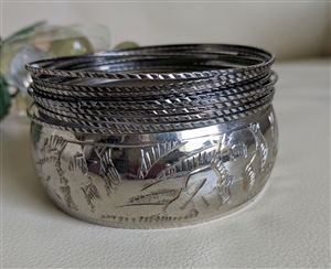 Eleven piece silver tone metal stacked bangle set featuring one thick etched floral bracelet and ten thin spacers