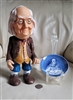 Vintage Benjamin Franklin plastic money bank next to a blue and white Enoch Wedgwood coaster from the 1970s