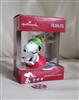Hallmark PEANUTS Snoopy molded plastic Christmas ornament wearing green hat and red scarf seated on red sled with box