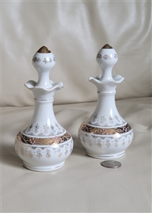 Detailed close-up shot of a matching vintage white porcelain vanity perfume bottle featuring an ornate ribbon-scalloped neck, bulbous body adorned with intricate hand-painted gold-tone scrollwork and raised enamel dots, and a matching pointed finial stopp