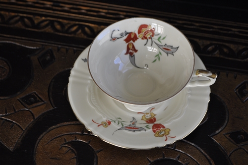 Vintage cream embossed porcelain teacup and saucer set with colorful floral pattern and gold trim