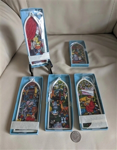 The front view shows a set of five Precious Moments porcelain ornaments shaped like cathedral windows with colorful illustrations of children and nature scenes. A close up shot reveals the script printed along the white porcelain edges and the official 19