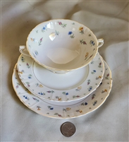 Three piece vintage Syracuse Suzanne porcelain set featuring a footed soup bowl saucer and dessert plate with multi color floral rims and gold accents