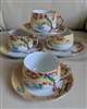 A group of four delicate Japanese teacups and saucers with colorful parrot designs, showing the translucent nature of the porcelain and gold toned handles