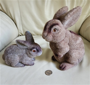 Two vintage 1970s bunnies with shimmering brown and silver flocked fur including a large money bank and a smaller toy sitting on a neutral surface with a coin for scale